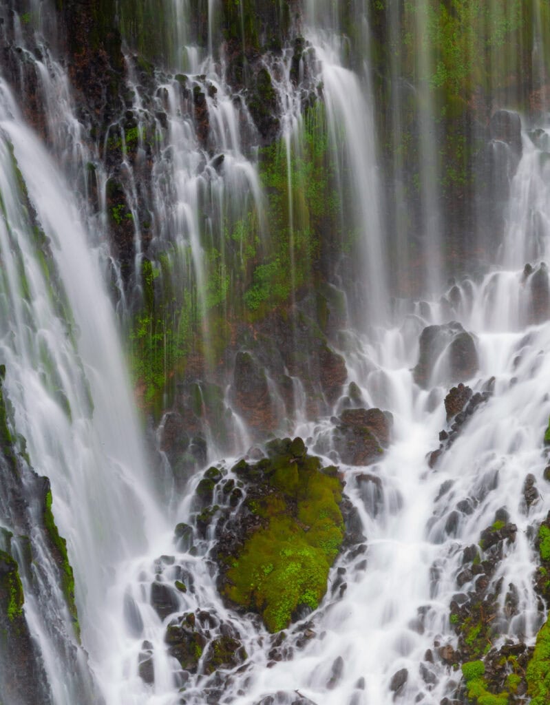 Vertical streams of water flowing down the moss-covered face of Burney Falls at McArthur-Burney Falls Memorial State Park, California