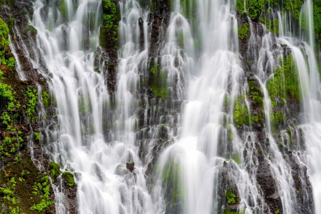 Close view of Burney Falls with white water streaming over dark rock and green moss at McArthur-Burney Falls Memorial State Park, California