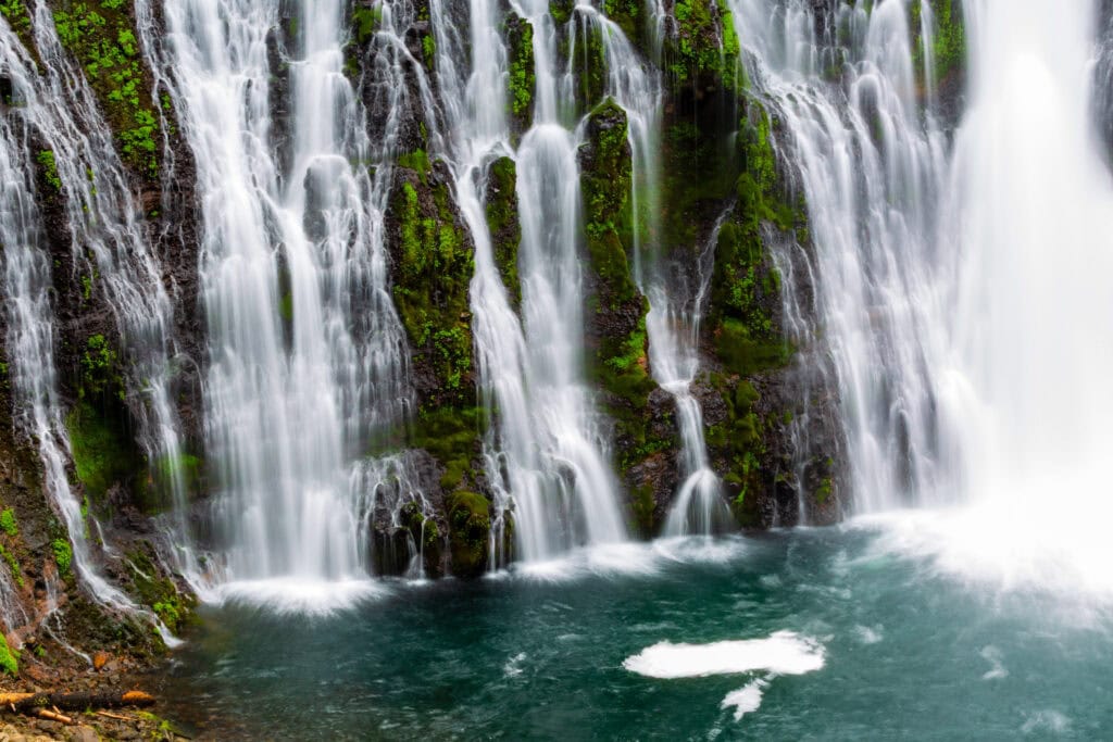 Burney Falls cascading into a turquoise pool surrounded by rocky shoreline at McArthur-Burney Falls Memorial State Park, California