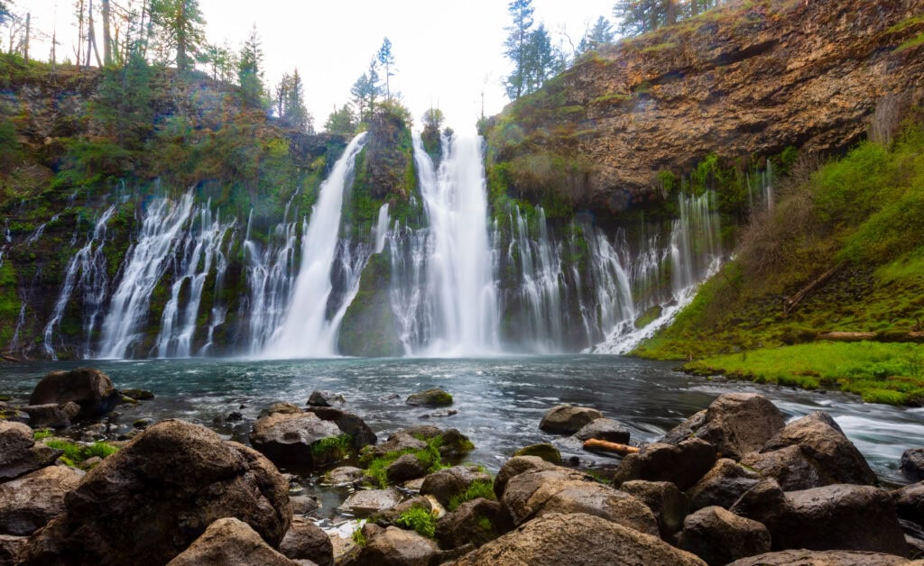 Burney Falls cascading into a turquoise pool surrounded by rocky shoreline at McArthur-Burney Falls Memorial State Park, California