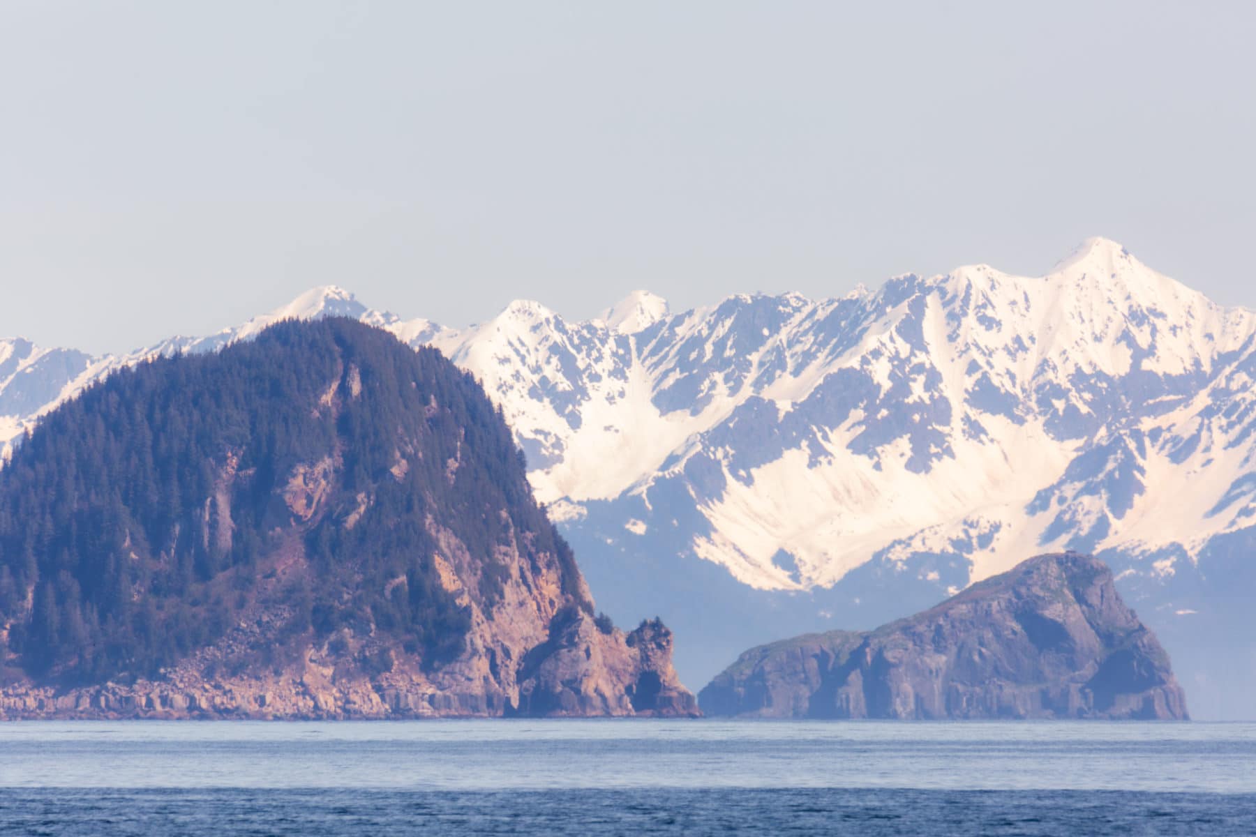 sea stacks in the kenai fjords with snowy peaks behind it