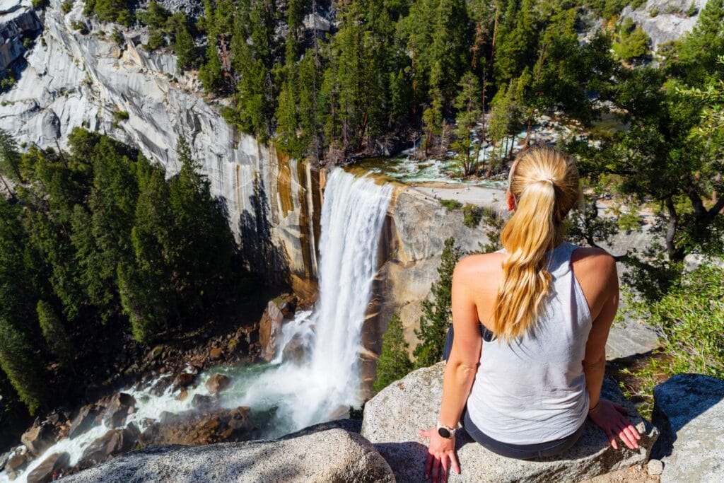 a female hiker looks down at vernal falls from clark point, one of the best hikes in yosemite national park