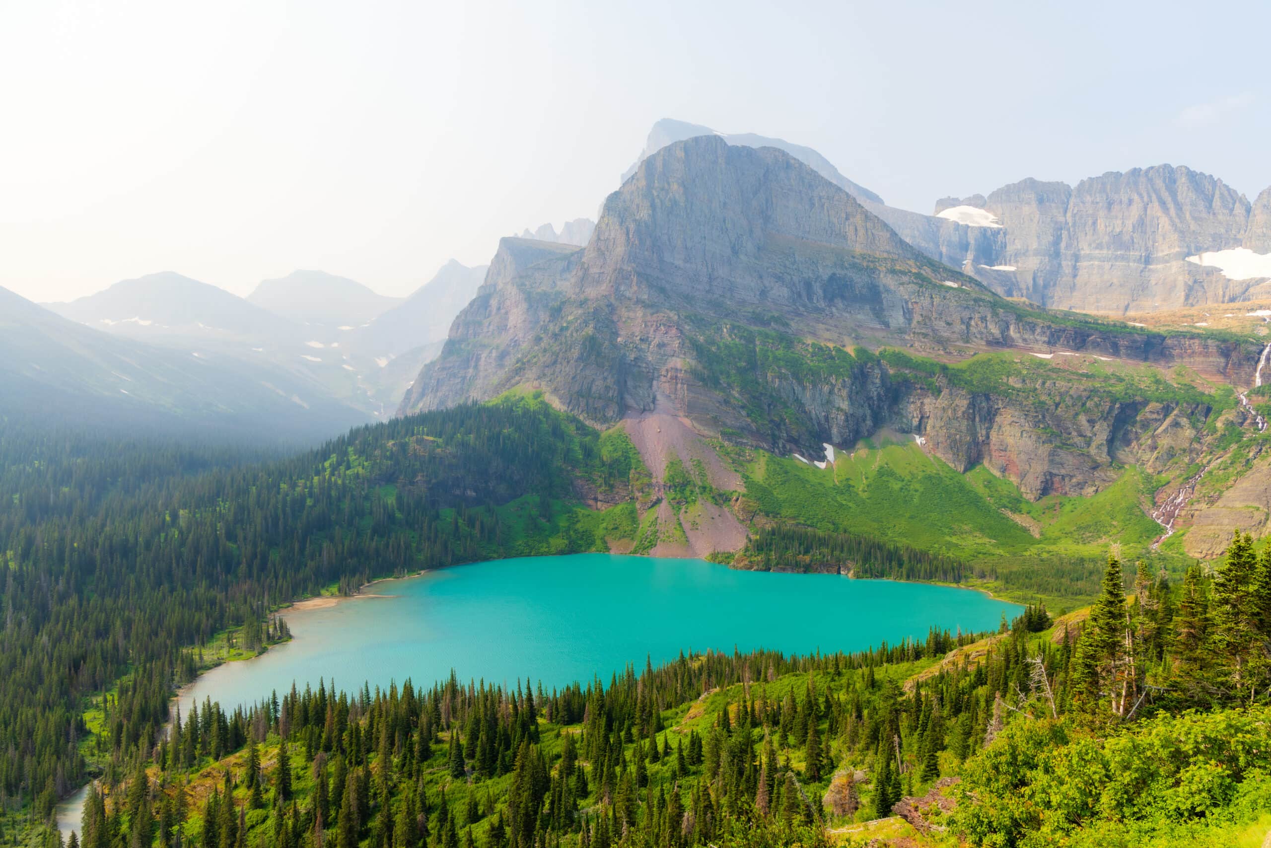 a turquois lake with mountains behind it on the grinnell glacier trail in glacier national park