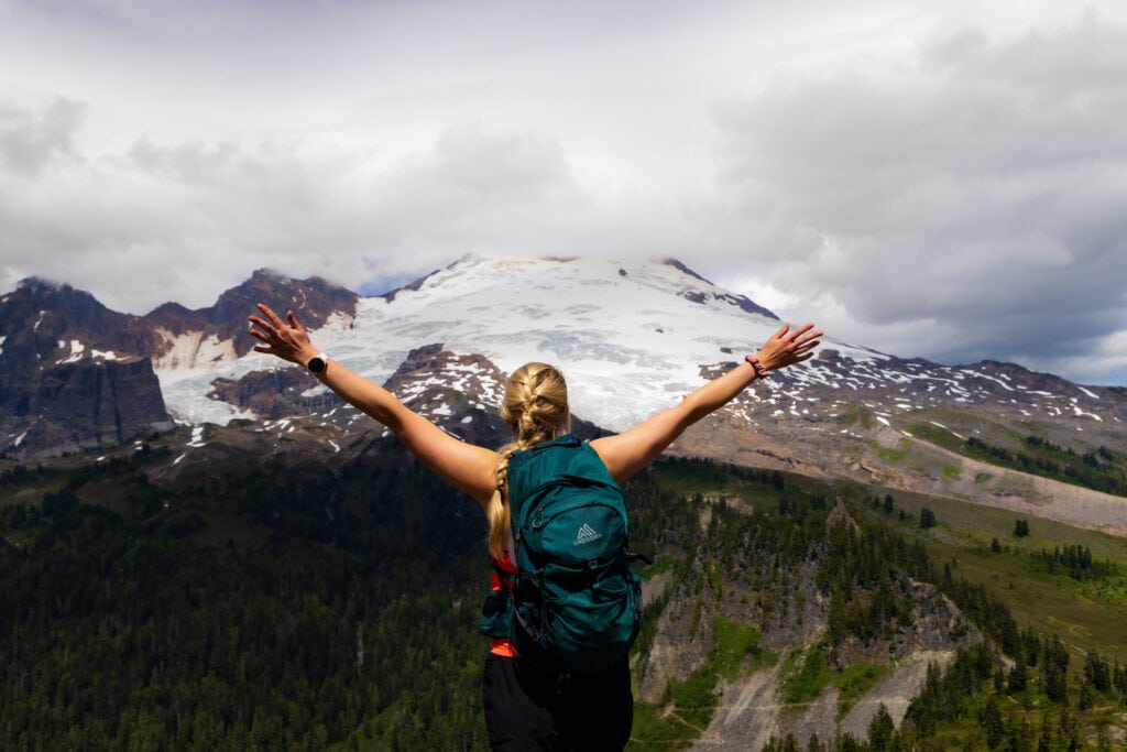 A hiker raises her arms in front of Mt. Baker. 