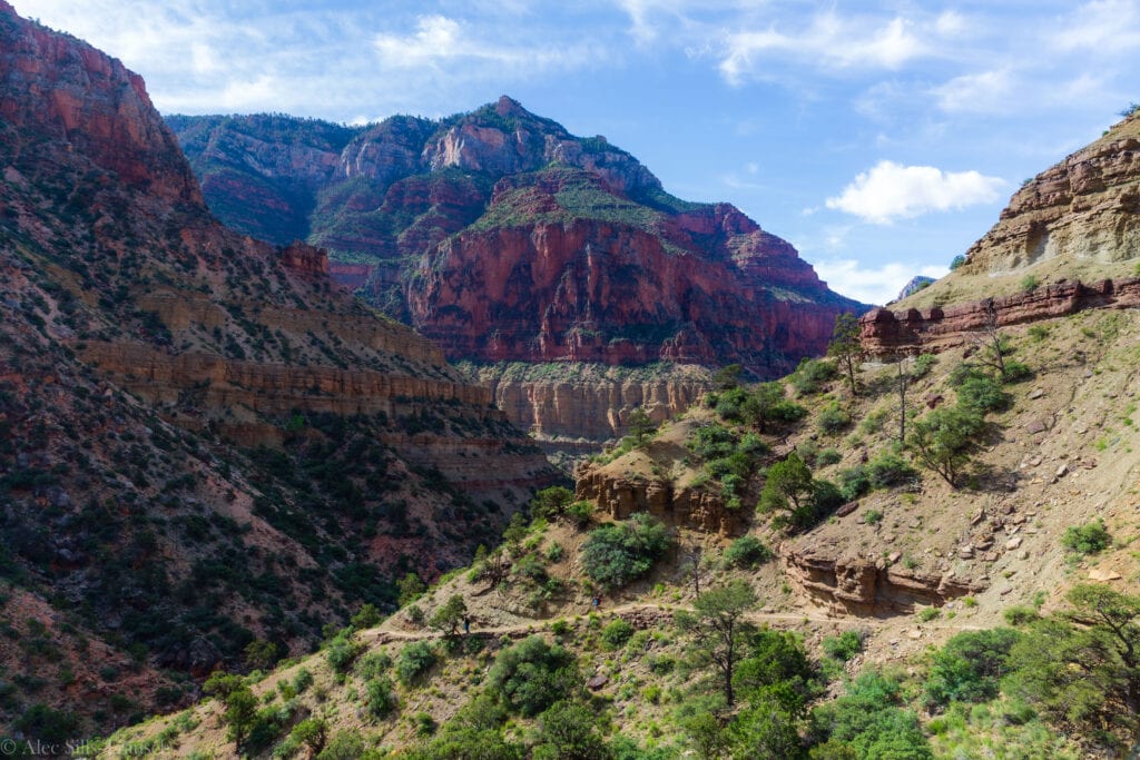 three hikers walk on the trail in the grand canyon with towering rocks above them