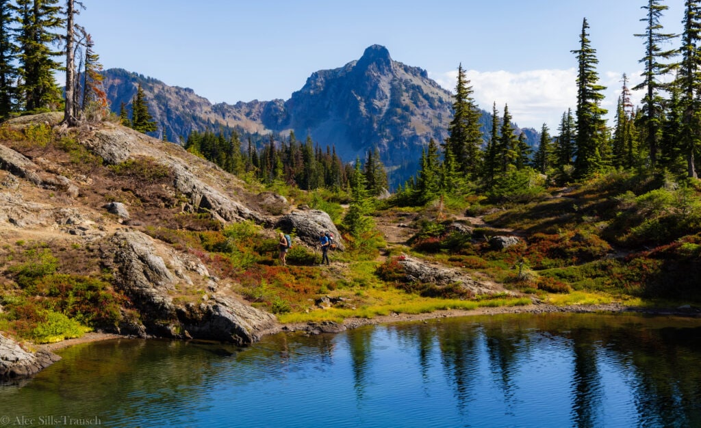 two hikers hike alongside a lake shore