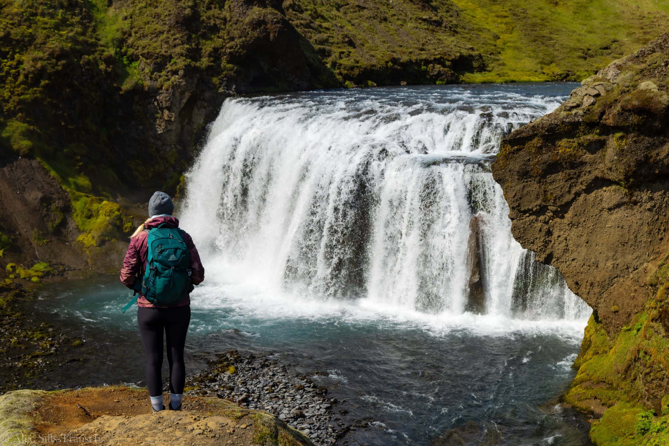 a hiker stares out at a waterfall on the skogafoss waterfall way hike