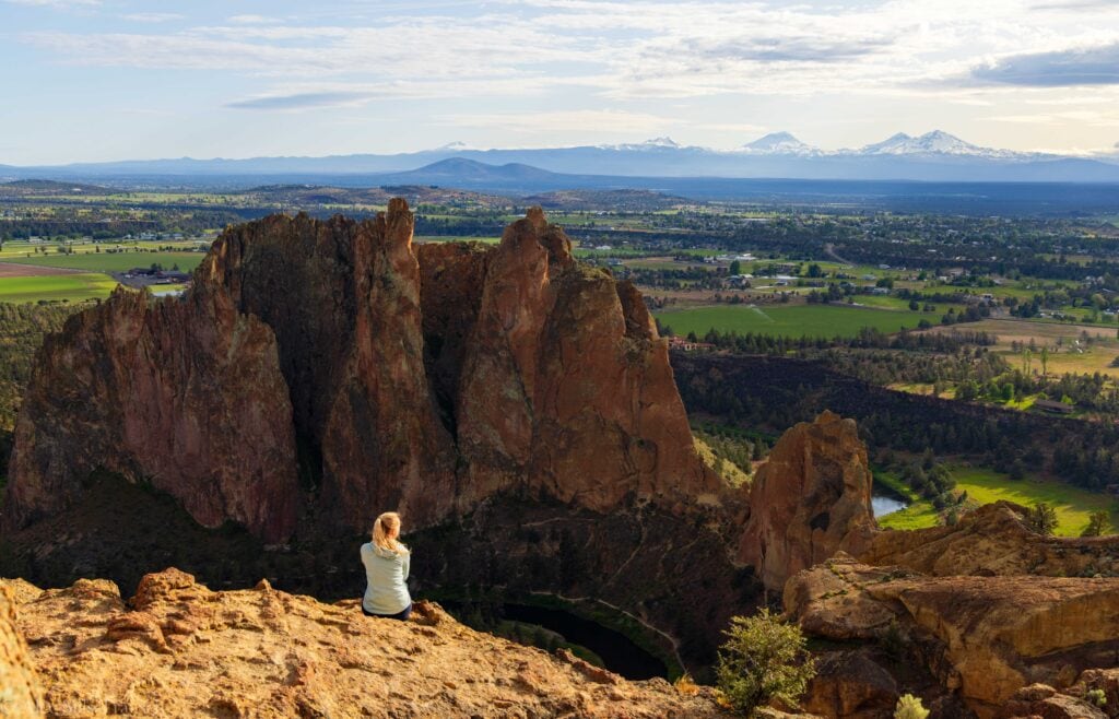 a woman sits on the rock at the top of smith rock state park in bend oregon