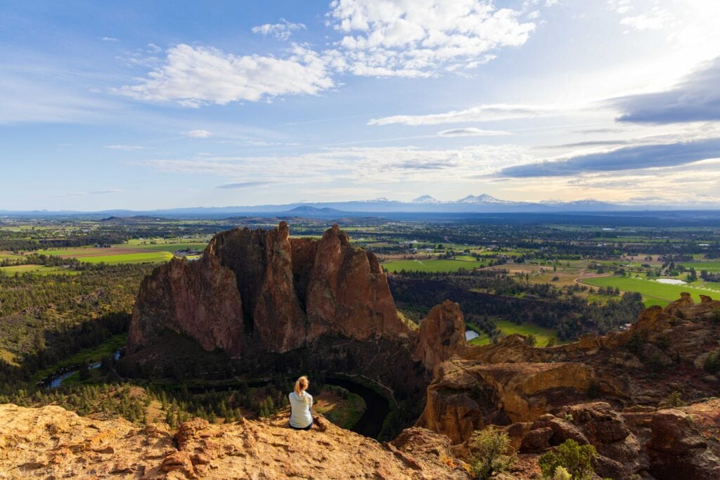 a hiker sits on the edge overlooking smith rock state park in oregon