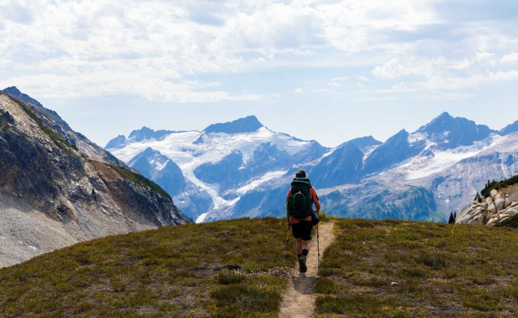 a hiker walks along a ridge line surrounded my mountains