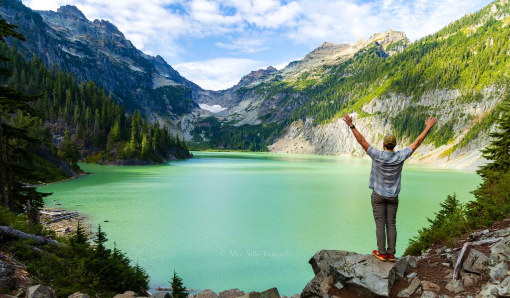 a hiker raises his arms as he looks out over blanca lake in the washington cascades