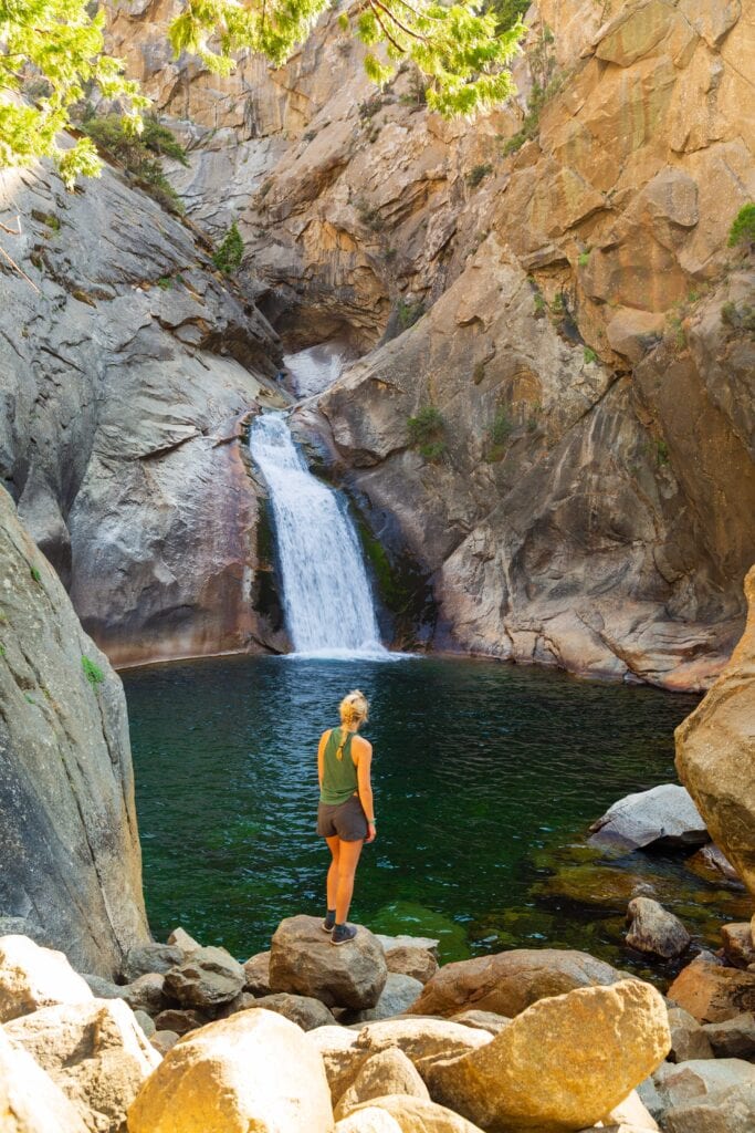 a woman stands in front of roaring river fall