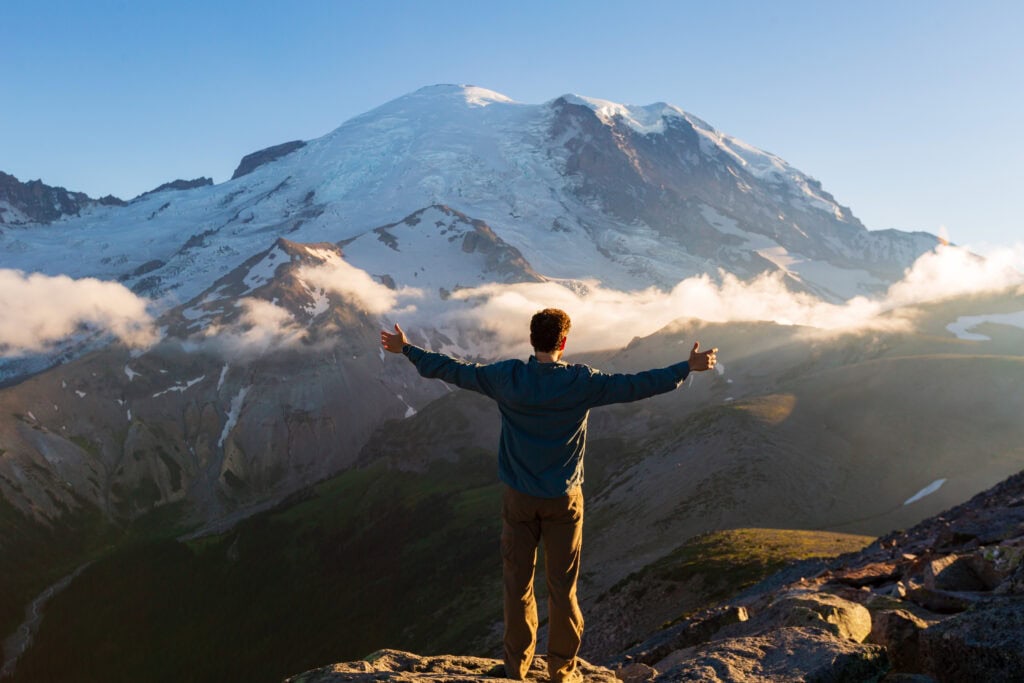 a man holds out his arms looking at a mountain