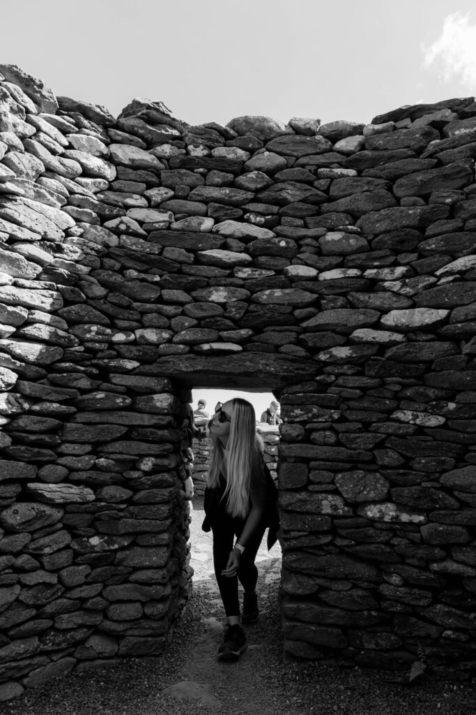 a woman walking through a small dooreway in the beehives. This is a must for any dingle peninsula itinerary in ireland.
