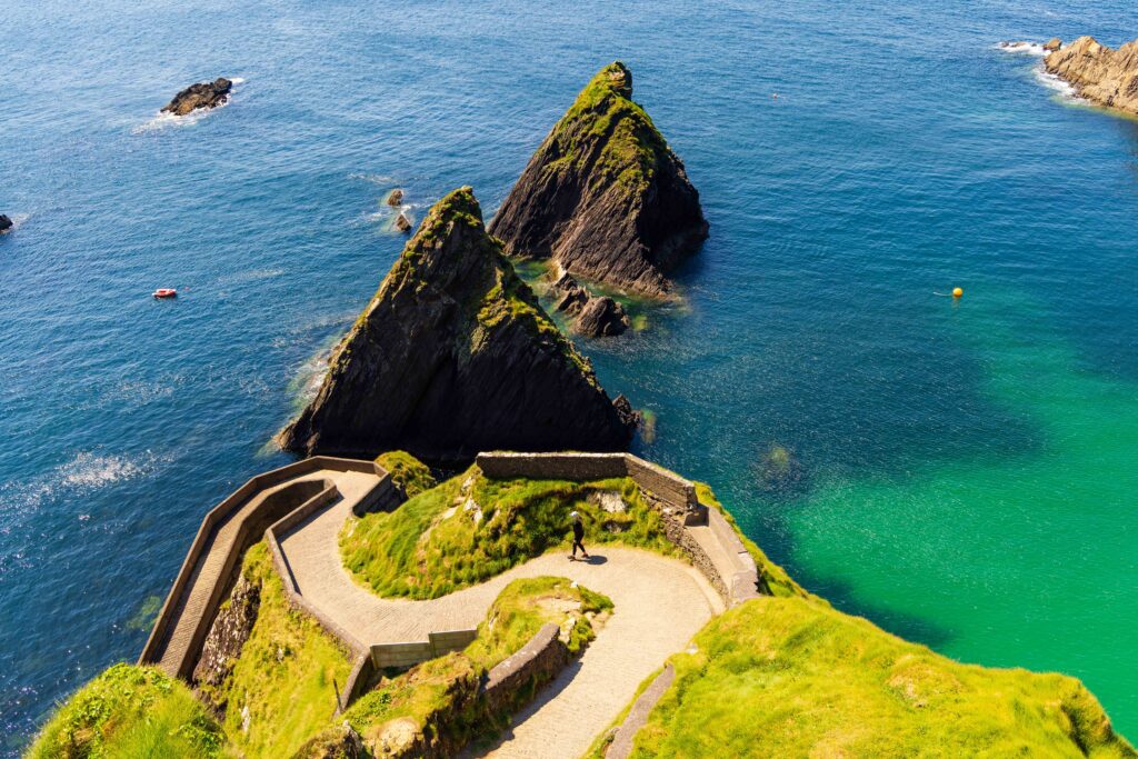 a tourist walks down the stone walkway on the dunquin pier. this is a must stop for your dingle peninsula itinerary