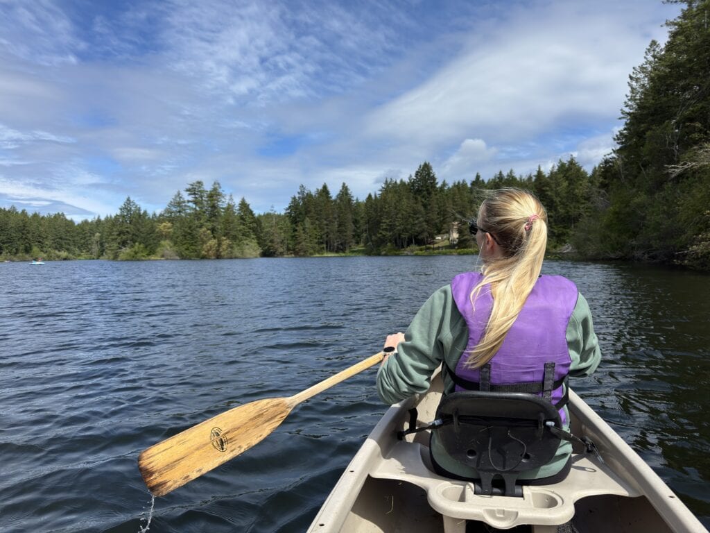 a female sits in the front of a canoe and paddles on a lake 
