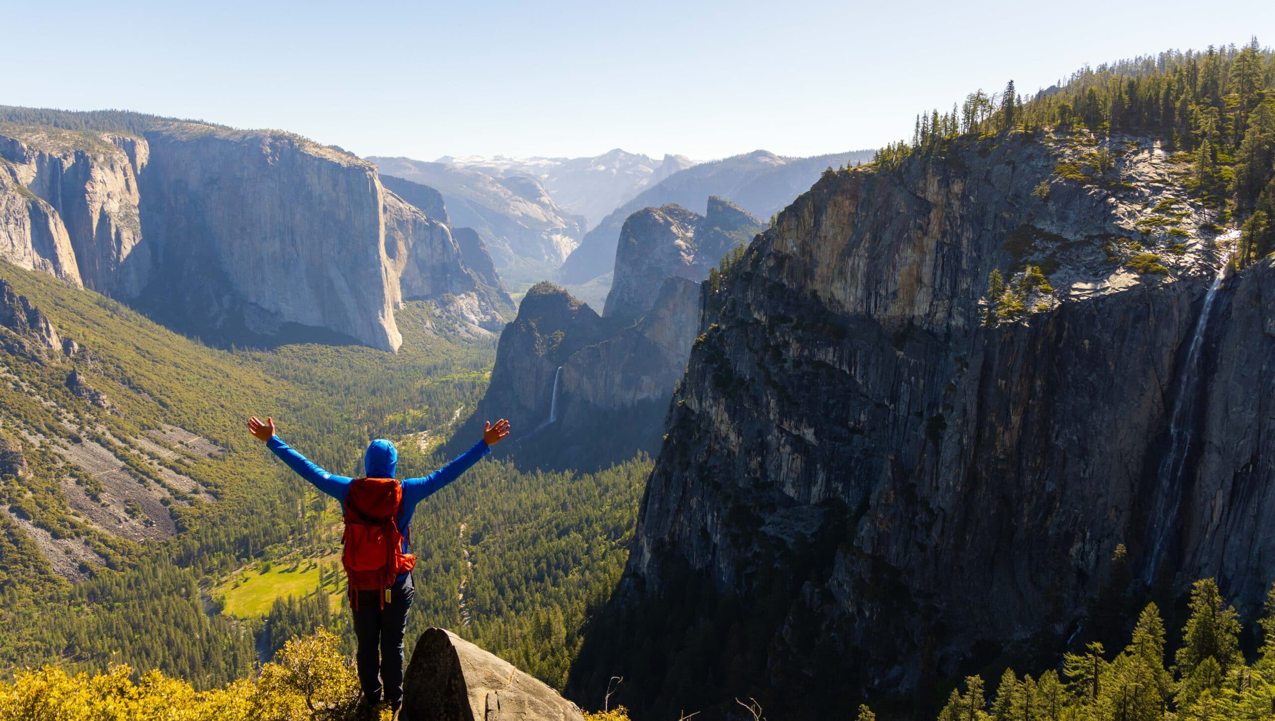 a hiker raises his arms at old inspiration point in yosemite