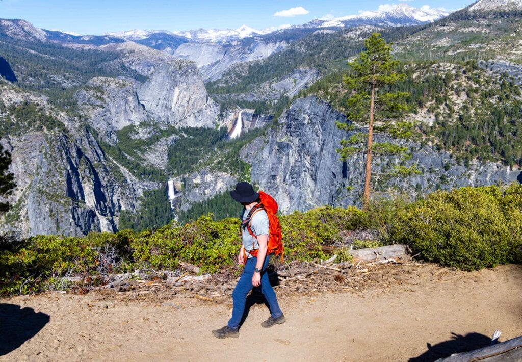 a hiker walks on illuehete falls trail in yosemite with waterfalls behind him