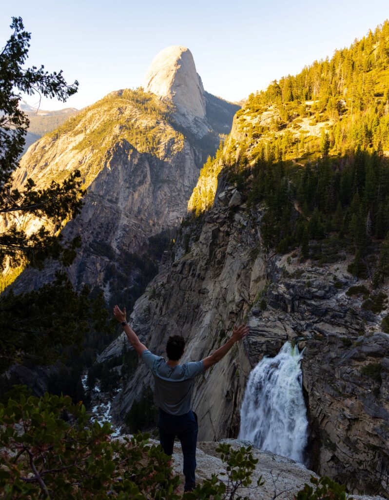 a hiker raises his arms near illuehete falls in yosemite