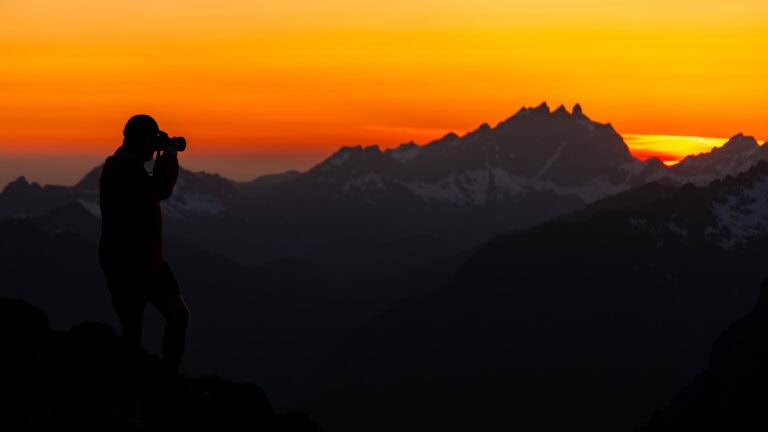 a hiker takes a photo during sunset on an edge