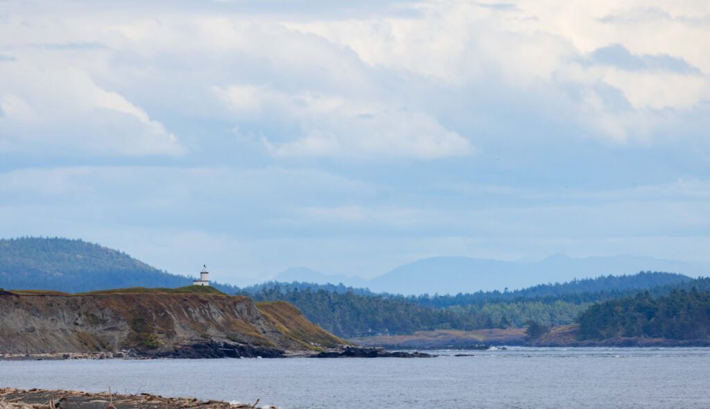 a lighthouse on a cliff edge in the distance with clouds above