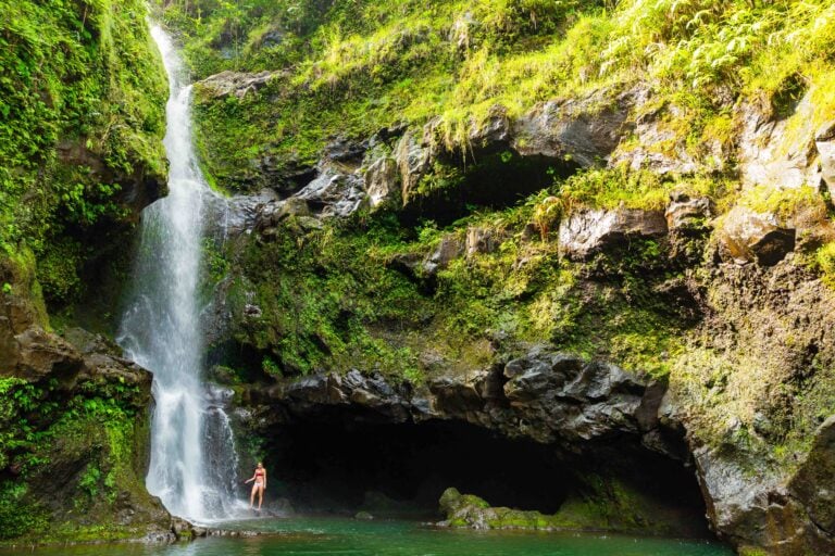 a female hiker stands near a waterfall in maui along the road to hana