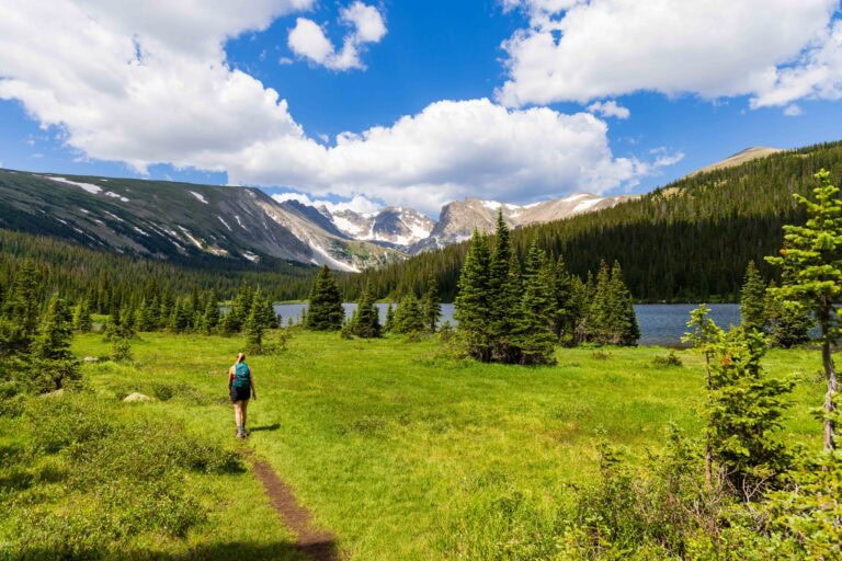 a hiker walks on a trail near a lake surrounded by trees