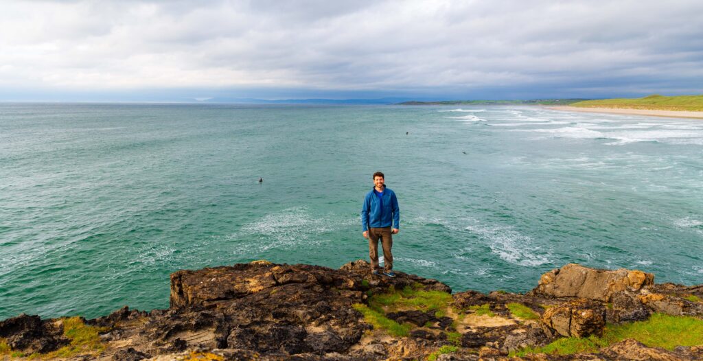 a male tourist smiles at the camera above the ocean