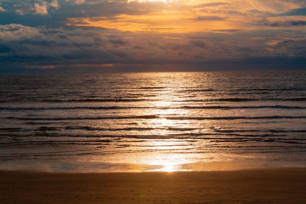 sunset colors on the beach with one surfer in the water