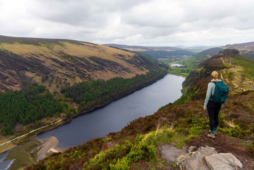 a female hiker looks out at a long lake below