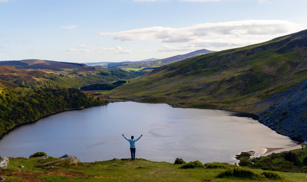 a hiker holds up his arms above a lake in ireland