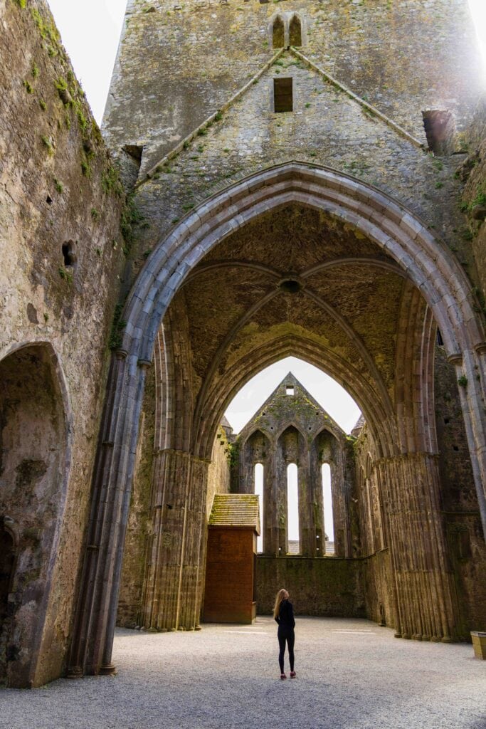 huge clumbs and arches inside the rock of cashel in ireland with a tourist standing below looking up