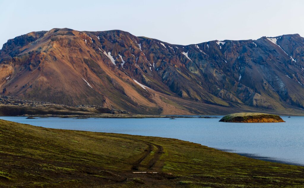 mountains and a lake with tire tracks heading away in the icelandic highlands