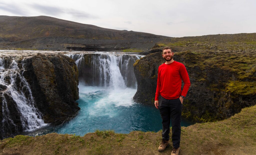 the author smiles at the camera wearing red with a waterfall behind him in the icelandic highlands.