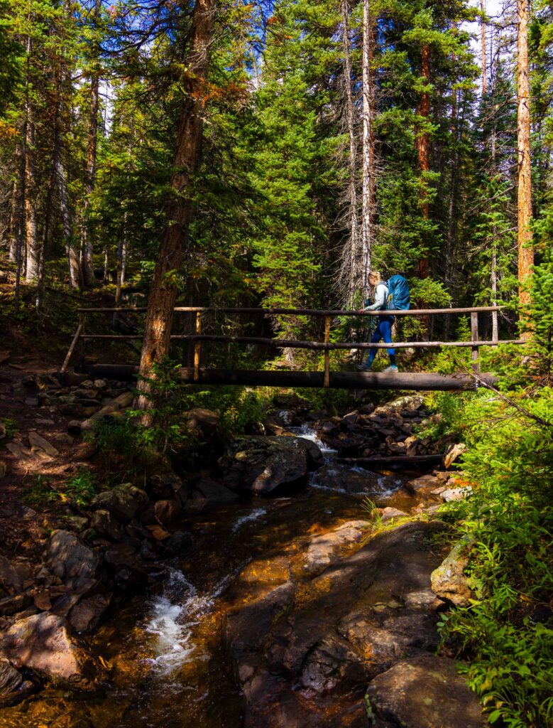 a hiker crosses a wooden bridge over a small creek