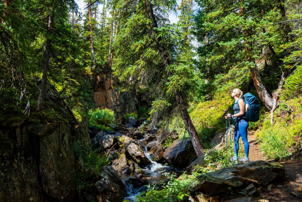 a female hiker with a backpack standing on a rock looking at a stream