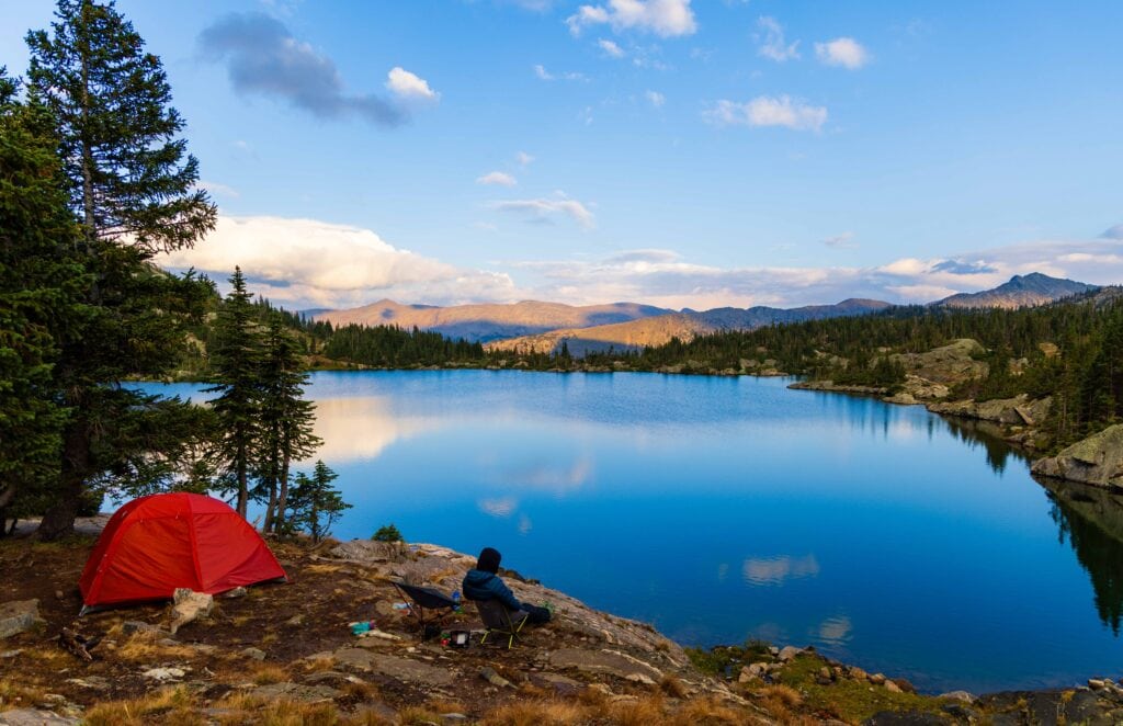 a female hiker sits in a chair overlooking missouri lake, there's a red tent to her left