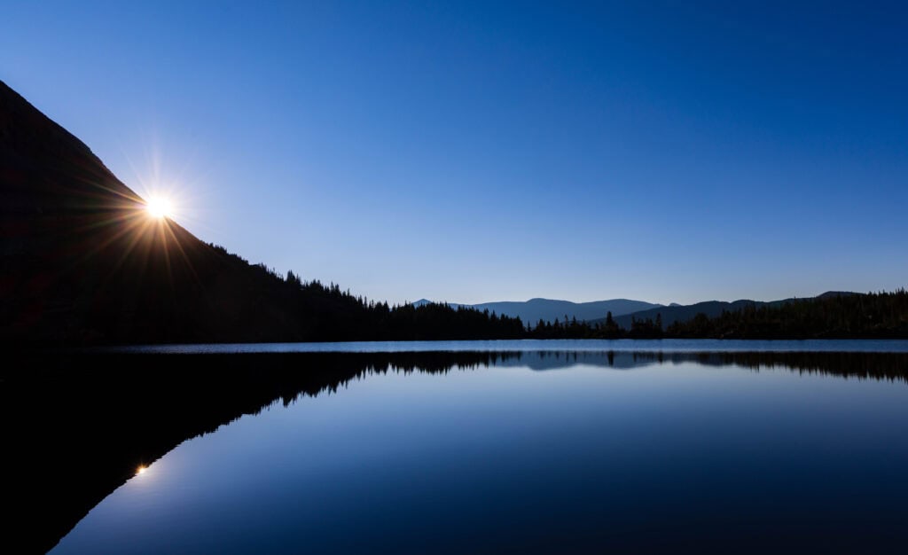 the lake with the sun coming up on the lefthand side of the image