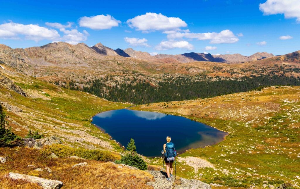 a woman stands on a rock looing at at treasure vault lake on the missouri lakes fancy lake loop