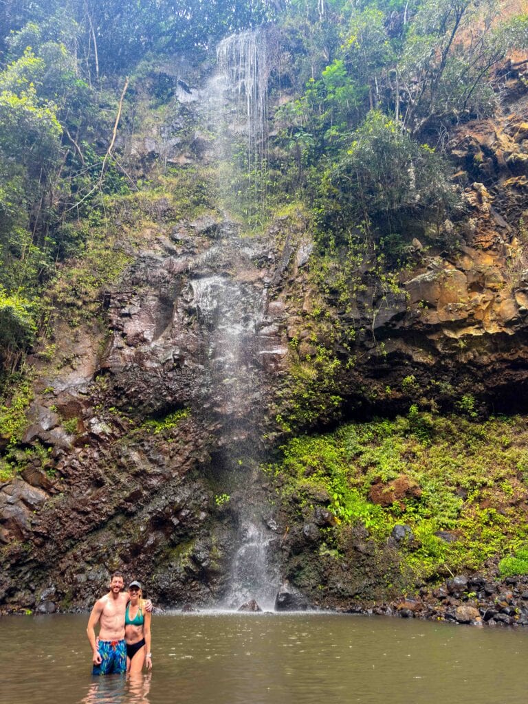 two guests on the secret falls kayaking tour smile at the camera with a waterfall behind them