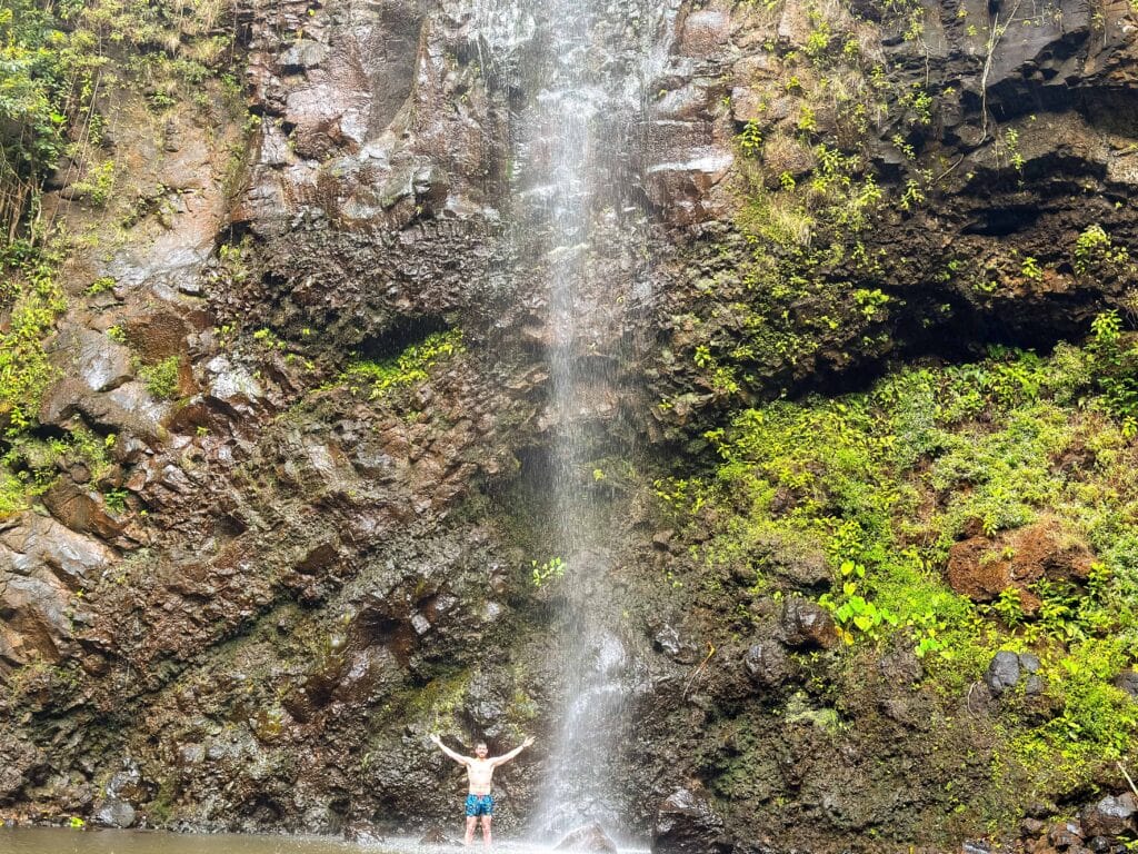 the author raises his hands above him as he stands under secret falls in hawaii