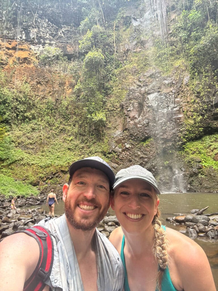 two hikers smile with secret falls behind them