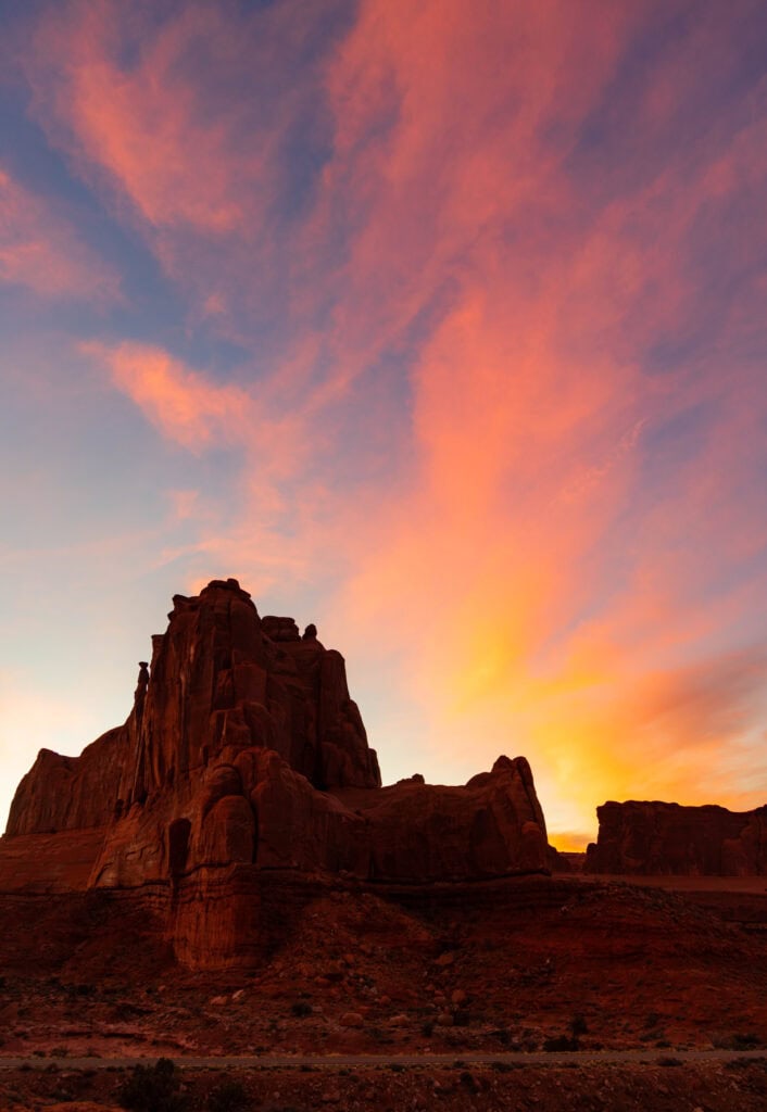 a towring red sandstone rock with sunset colors behind it