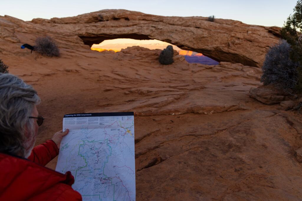 a hiker looks at a map at mesa arch in canyonlands national park