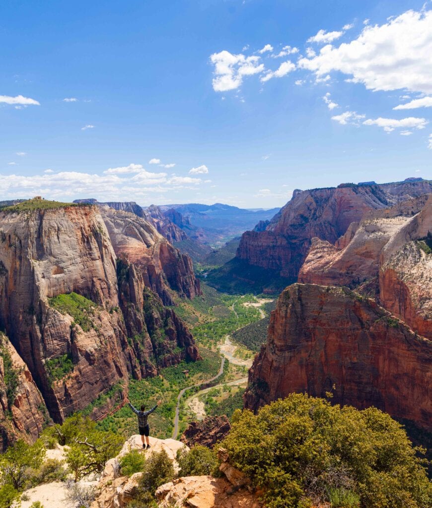 a hiker stands on the edge below observation point in zion national park