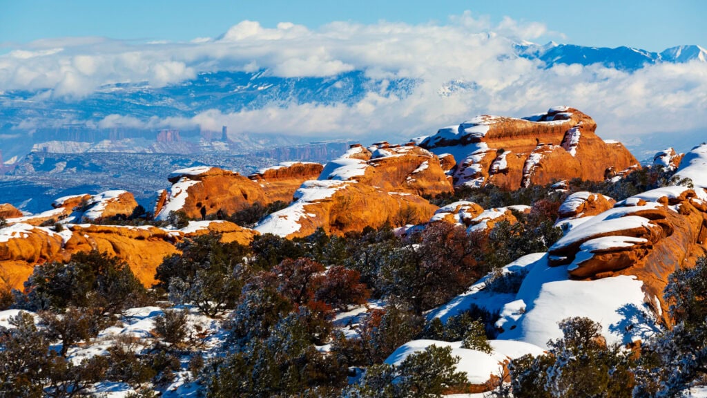 snow on top of the red rock in archs national park with bushes around