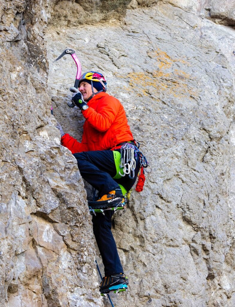 a climber on a rock wall with crampons and an ice axe