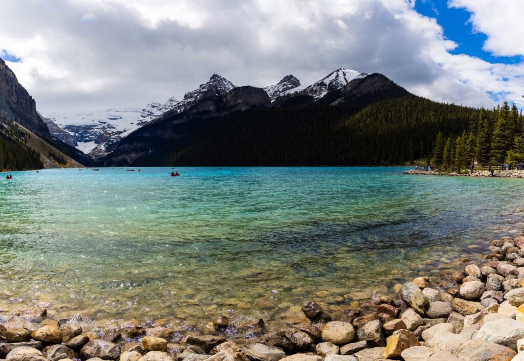 the rocks along lake louise with a canoe in the water and mountains in the background