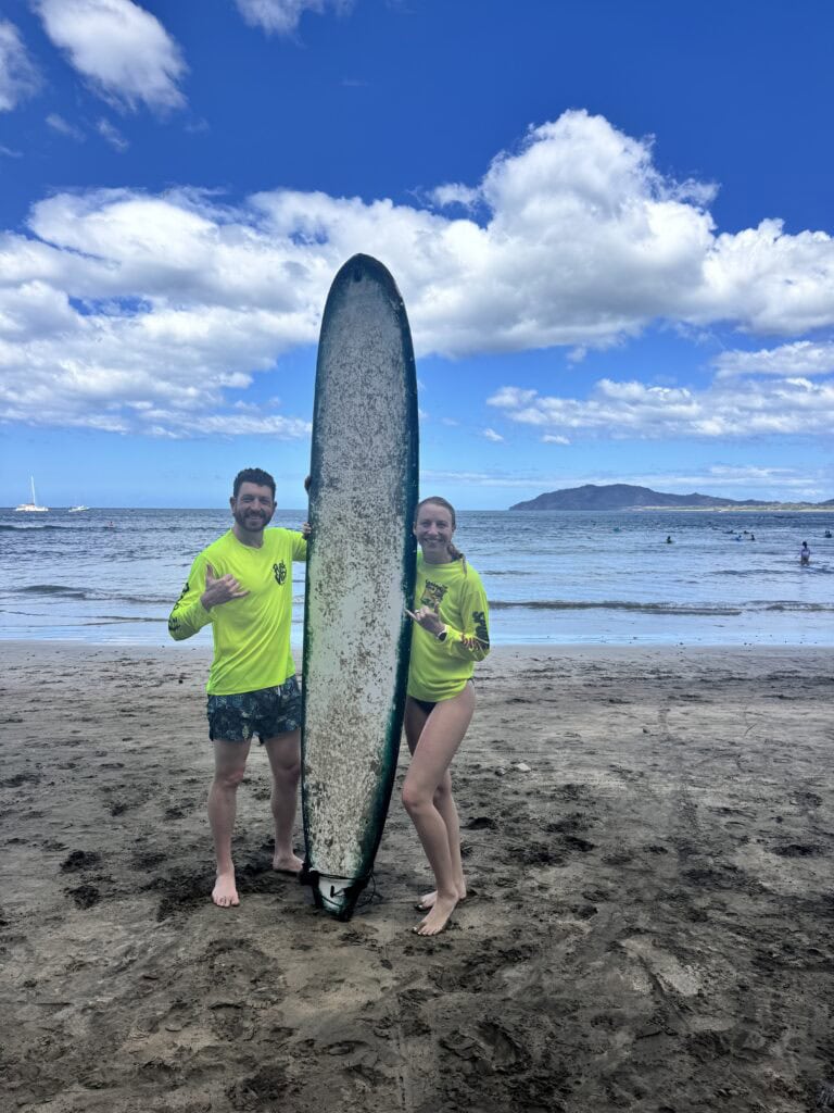 a man and woman stand near a surfboard after surf lessons in costa rica