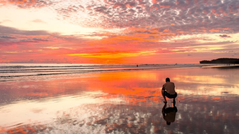 a photographer crouches on the beach during sunset